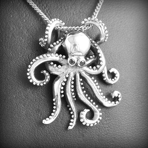 Pendentif pieuvre en argent, deux tentacules servent de bélière, les yeux sont en zirconium noir,...